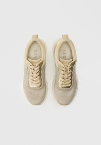 Sneakers beige lavorate a maglia con tomaia testurizzata, design con lacci, imbottitura morbida e suola in gomma. Il marchio è visibile sulla linguetta.