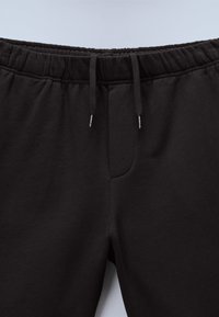 Μαύρο φούτερ παντελόνι με ελαστική μέση και κορδόνια, με διακριτική ραφή στο μπροστινό μέρος.