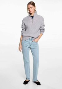 Svetlosivý rebrovaný pulóver s polovičným zipsom na golieri, skombinovaný so svetlomodrými džínsami s rovnými nohavicami a čiernymi šľapkami. Celkový vzhľad je hladký.