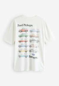 Valkoisesta puuvillapaidasta, jossa on erilaisia Ford-pickup-tehtaita eri väreissä. Teksti "Ford Pickups. Ja nyt..." ylhäällä ja alhaalla.