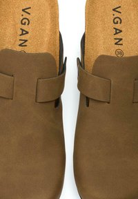 Brown vegan leather sandals with a cork insole. Features a wide strap with a buckle and rounded toe shape. Soft textured surface.