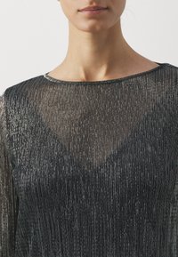 Svart, gjennomsiktig topp med vertikale sølvstriper, rund hals og lange ermer med en glatt, litt teksturert overflate.