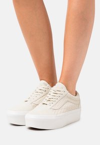 Białe zamszowe tenisówki z plecionymi detalami po bokach, płaskie białe gumowe podeszwy i płaskie sznurowanie. Minimalistyczny design bez zdobień.