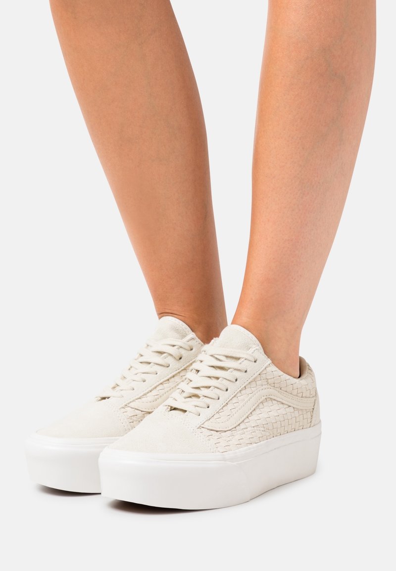 Białe zamszowe tenisówki z plecionymi detalami po bokach, płaskie białe gumowe podeszwy i płaskie sznurowanie. Minimalistyczny design bez zdobień.