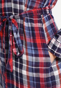 Robe en coton à carreaux rouge, marine et blanc. Elle présente une ceinture à nouer, des manches courtes et des poches, avec un tissu léger et texturé.