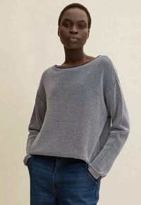 Maglione grigio lavorato a maglia con una vestibilità ampia, scollo a barco, maniche lunghe e motivo a trama, abbinato a jeans blu scuro.
