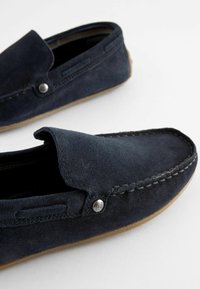 Marineblaues Wildleder-Loafers mit gestepptem Design, kontrastierender hellbrauner Gummisohle und silbernem Akzentknopf an der Seite.
