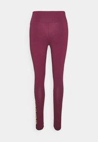 Maroon leggings with a high waistband, made of stretchy fabric. Features a golden logo accent on the left leg. Smooth texture.
