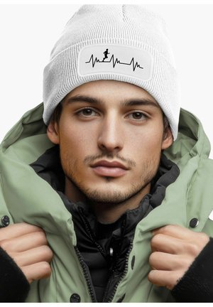White ribbed beanie with a black heartbeat graphic and a runner silhouette on a rectangular patch; worn with a green parka jacket.