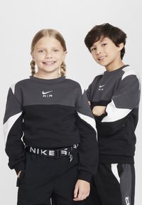 Črne in sive športne majice z belimi detajli in logotipom "AIR". Obe osebi nosita usklajen temne hlače in črn pas z napisom "NIKE".