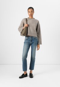 Harmaa, lyhythihainen neule, jossa on leveät hihat, siniset skinny-farkut ja mustat loafer-kengät. Pidessä pehmeää, oliivinvihreää käsilaukkua. Yksinkertainen, moderni ilme.