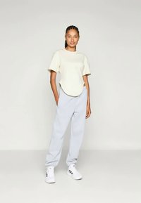 Svetlo bež majica oversize in svetlo sivi trenirki, v kombinaciji z belimi supergami z črnimi detajli. Gladek material z enostavnim dizajnom.