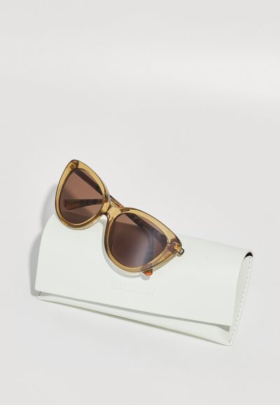 Cat-eye sunglasses with amber frames and brown lenses, resting on a white case embossed with "Burberry." Smooth texture, minimalistic design.
