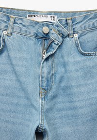Jeans de denim azul claro con un diseño de pierna recta, cierre con cremallera, botón de metal y costuras naranjas. La etiqueta muestra las tallas W 27 y L 32.