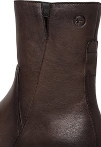 Bottine en cuir marron avec texture lisse, coupe droite et détails cousus. Présente un logo discret sur le côté.