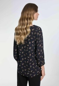Granatowa bluzka z kwiatowym wzorem w jasnobrązowym kolorze, z rękawami 3/4 i luźnym krojem. Gładki materiał z delikatnym połyskiem.