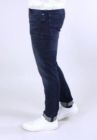 Ciemnoniebieskie dżinsy o wąskim kroju, z klasycznym projektem pięciu kieszeni i podwiniętymi nogawkami, zestawione z białymi trampkami.