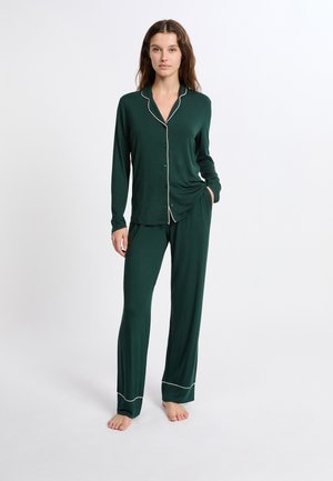 Conjunto de pijama verde hecho de tela suave; camisa de manga larga con ribete blanco, cierre de botones en el frente y pantalones a juego con piernas rectas y dobladillos ribeteados.