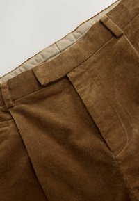 Pantaloni din corduroy maro cu o suprafață texturată, având o croiala dreaptă și pliseuri cusute în față. Talie cu o căptușeală dintr-un material mai deschis.
