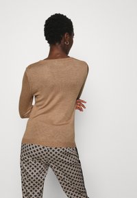 Maglione marrone a maglia con scollatura rotonda e maniche lunghe, abbinato a pantaloni neri e crema a fantasia con un design geometrico.