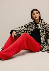Zwart-wit gestreepte nepbontjas met een zwarte rand, gecombineerd met rode, wijde gebreide broek. Zwarte sneakers met witte accenten.