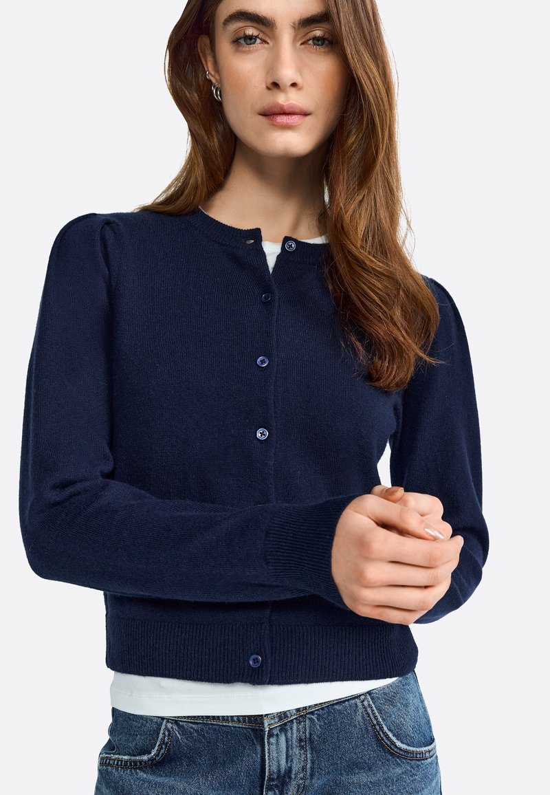 Marineblaue Strickjacke mit langen Ärmeln, gerippten Bündchen, rundem Halsausschnitt und Knopfverschluss; weiche Textur und taillierte Silhouette.