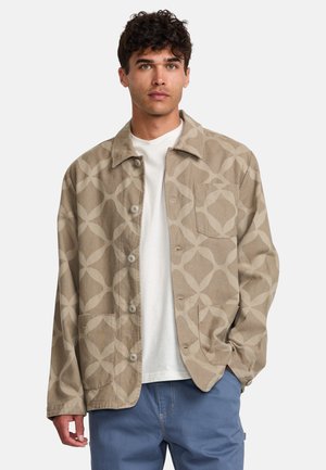 Beige jacket with abstract pattern, button closure, two front pockets, and a relaxed fit, worn over a white shirt.