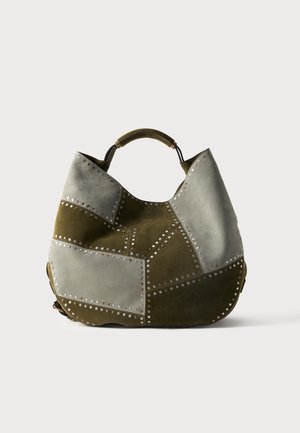 Sac hobo avec un motif patchwork en daim olive et gris clair, décoré de clous métalliques ronds et d'une courte poignée supérieure.