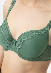 Bra verde in pizzo con design imbottito. Presenta un bordo in pizzo floreale, spalline regolabili e un dettaglio a fiocco centrale. Texture liscia in tutto il capo.