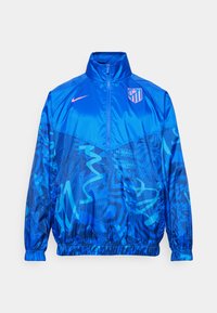 Giacca a vento blu con zip a metà, polsini elasticizzati, motivi astratti blu scuro e un logo sul petto. Realizzata in un tessuto liscio e resistente.