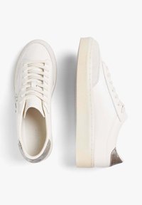 Zapatillas blancas de cuero con cordones, suela beige y detalle en ante plateado en el talón, mostradas desde vistas superior y lateral.