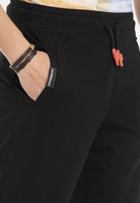 Zwarte sweatpants van zachte stof, met een zijzak met een logo-label, een verstelbaar trekkoord met rode accenten en een ontspannen pasvorm.