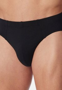 Slip in cotone nero con una texture liscia, vestibilità aderente e ampia vita in elastico. Il design presenta un taglio classico e cuciture minimali.