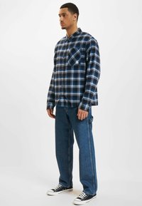 Gombos flaneling ing navy és kék pöttyös mintával, hosszú ujjakkal, egyetlen mellzsebbel. Laza fazonú kék farmernadrággal és fekete tornacipővel párosítva.