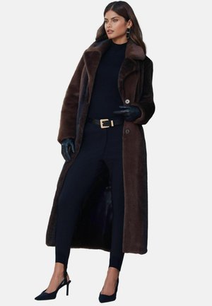 Brūns mākslīgās kažokādas mētelis ar lielu apkakli, melns pieguļošs turtlenecks un piegriezti bikses. Spīdīgas melnas cimdi un augstpapēžu kurpes papildina izskatu.