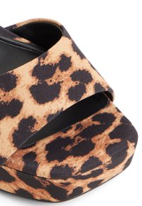 Sandalia de plataforma con estampado de leopardo y una tira ancha, con un tejido texturizado en tonos de beige y negro. Punta redondeada y tacón grueso.