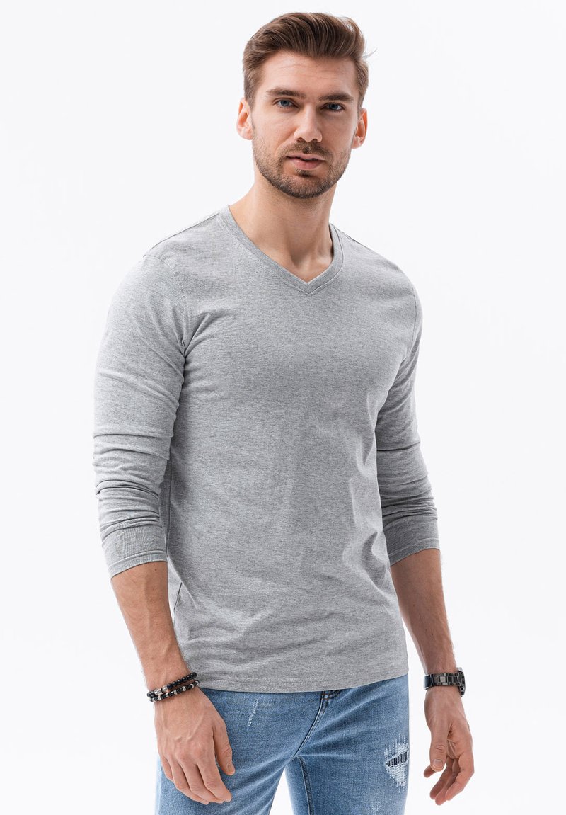 Grå långärmad t-shirt med V-hals i mjukt tyg, med ribbade ärmslut och en avslappnad passform. Kombinerad med slitna blå jeans och accessoarer.