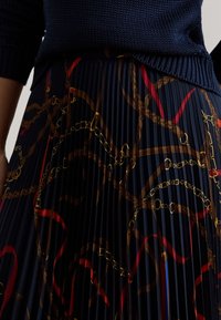 Marineblauer, plissierter Rock mit einem dekorativen Muster aus goldenen Ketten sowie roten und braunen Akzenten, gefertigt aus strukturiertem Stoff mit kunstvollen Designelementen.