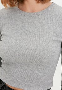 Grå ribbad långärmad topp med rund halsringning och åtsittande silhuett, tillverkad av mjukt, texturerat material. Minimalistisk design med en enkel finish.