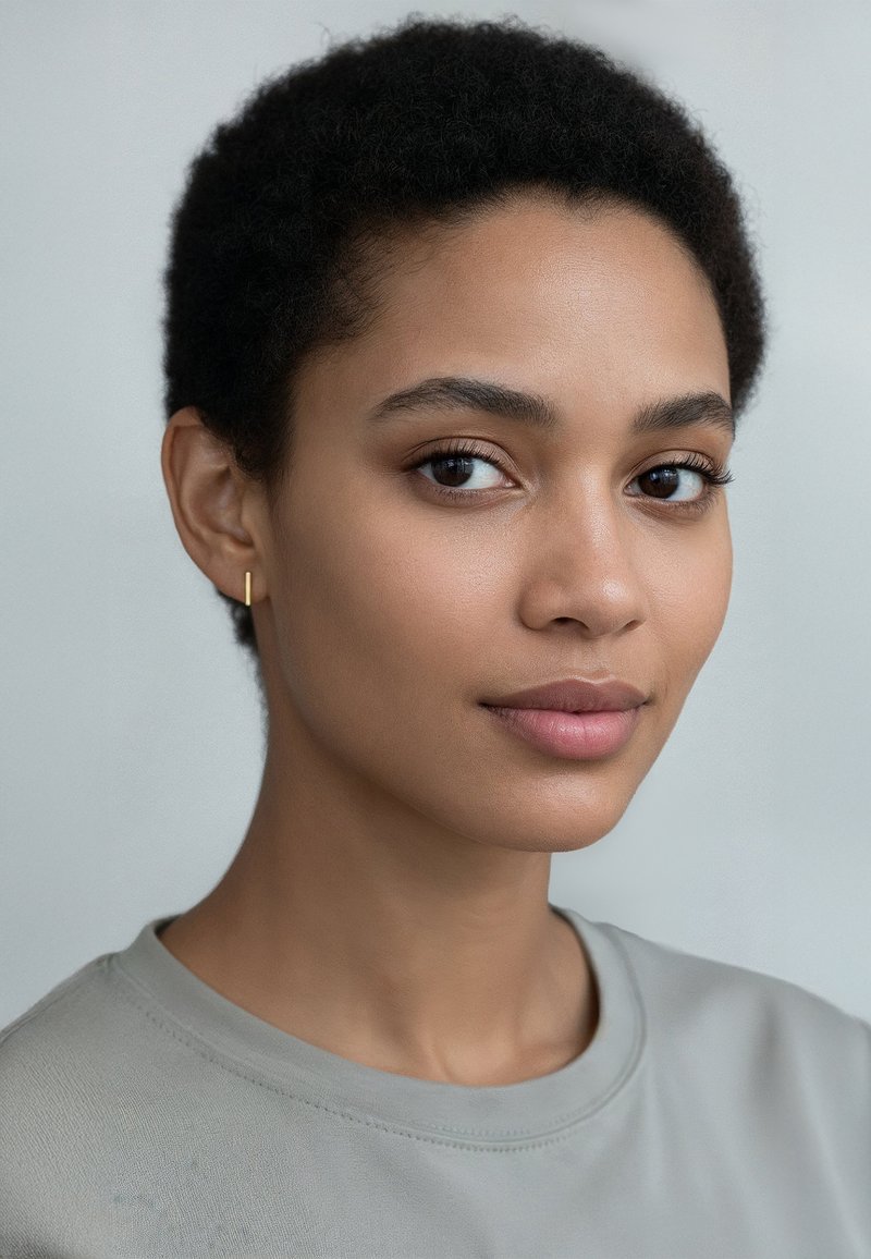 Haut gris clair à manches courtes avec un col rond. Texture lisse et douce. Le sujet a les cheveux courts et bouclés de couleur noire et un petit hoop en or.