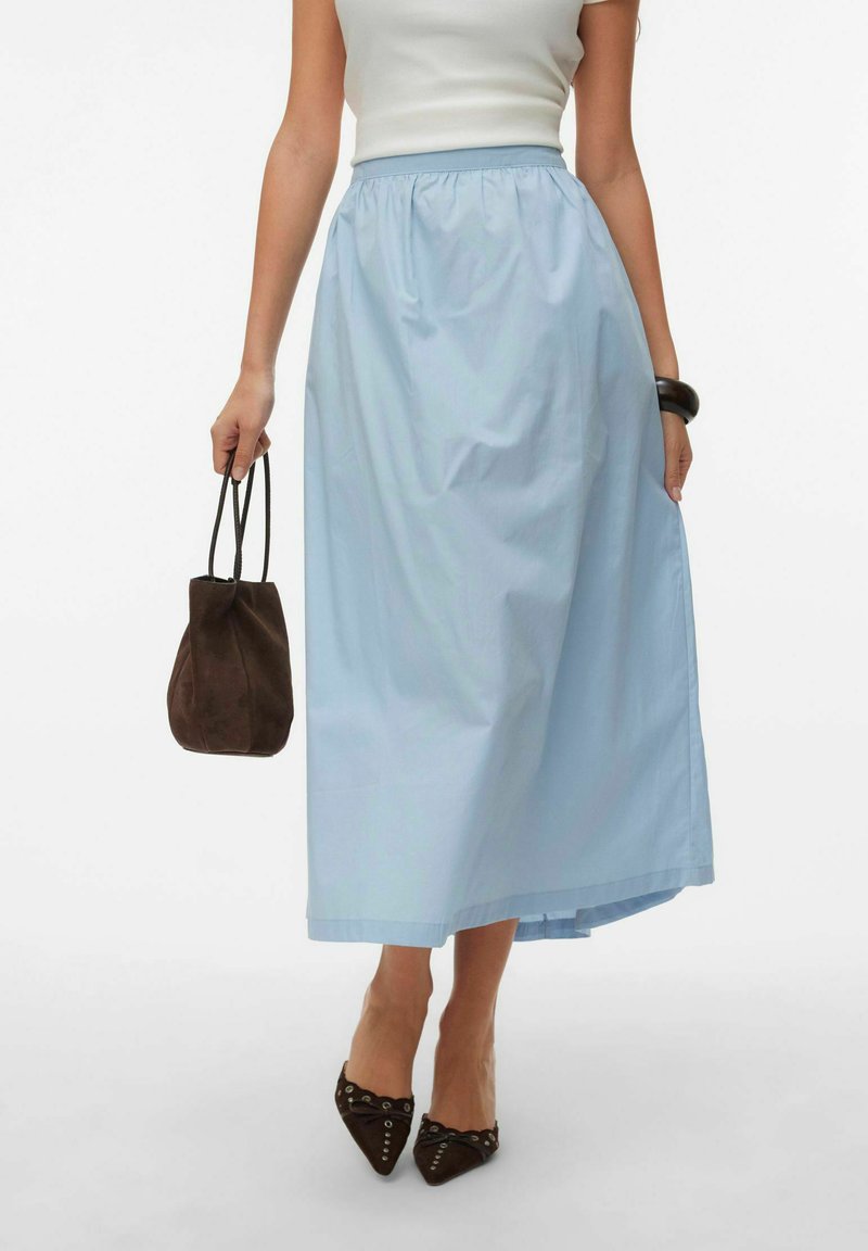 Lyseblå maxinederdel lavet af blødt stof med elastik i taljen. Kombineret med en mørkebrun ruskindstaske og spidse sko.