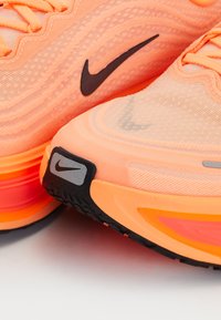 Nahaufnahme von orangefarbenen Nike-Laufschuhen, die die schwarzen Swoosh-Logos und die mehrlagige Sohle mit roten und orangefarbenen Akzenten hervorhebt.