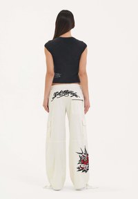 Zwarte cropped top en crème cargobroek met grafische ontwerpen. De cargobroek heeft zakken en trekkoorden bij de enkels.