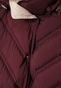 Bordeaux pufferjakke med quiltet design, knappelukning og lys foring med justerbare snore. Blødt, struktureret stof.