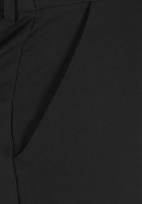 Svarta byxor i tyg med en slät textur, som har en subtil plissering framtill. Midjebandet är strukturerat och sitter vid midjan.