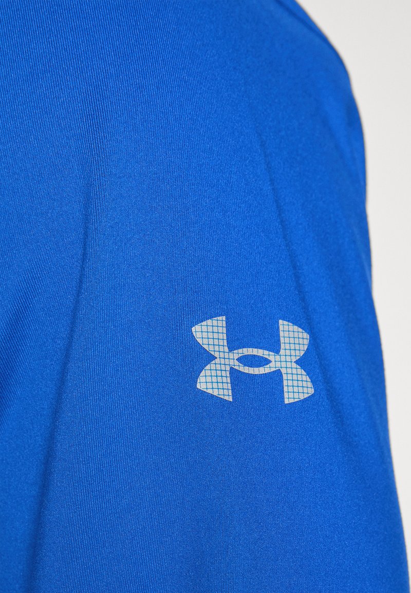 Camisa atlética azul con una textura suave, que presenta un logo de patrón de cuadrícula gris claro en la manga izquierda.