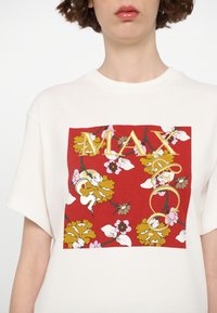 T-shirt bianco a maniche corte con una grafica floreale rossa e la scritta "MAX" ricamata in oro. Fiori gialli, rosa e bianchi con elementi decorativi.