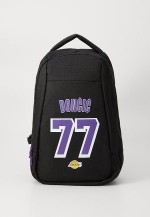 Sac à à dos noir avec des accents violets, portant le nom "DONČIĆ" et le numéro "77" imprimés en blanc gras. Comprend le logo des Lakers sur le côté.