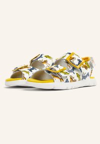 White sandals with colorful animal prints in yellow, green, and blue. Features adjustable velcro straps and a cushioned yellow sole.