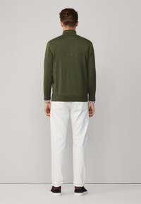 Pullover lavorato a maglia verde oliva con colletto, pantaloni bianchi e scarpe da ginnastica scure. Presenta un dettaglio a righe in contrasto sul colletto.